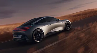 Peugeot RCZ Vision gris visto desde atrás en tres cuartos mientras circula por una carretera, con luces traseras rojas horizontales y techo oscuro.