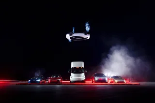 Tesla Roadster blanco suspendido boca abajo con estelas de gas visibles, sobre una fila de vehículos Tesla durante una demostración nocturna.