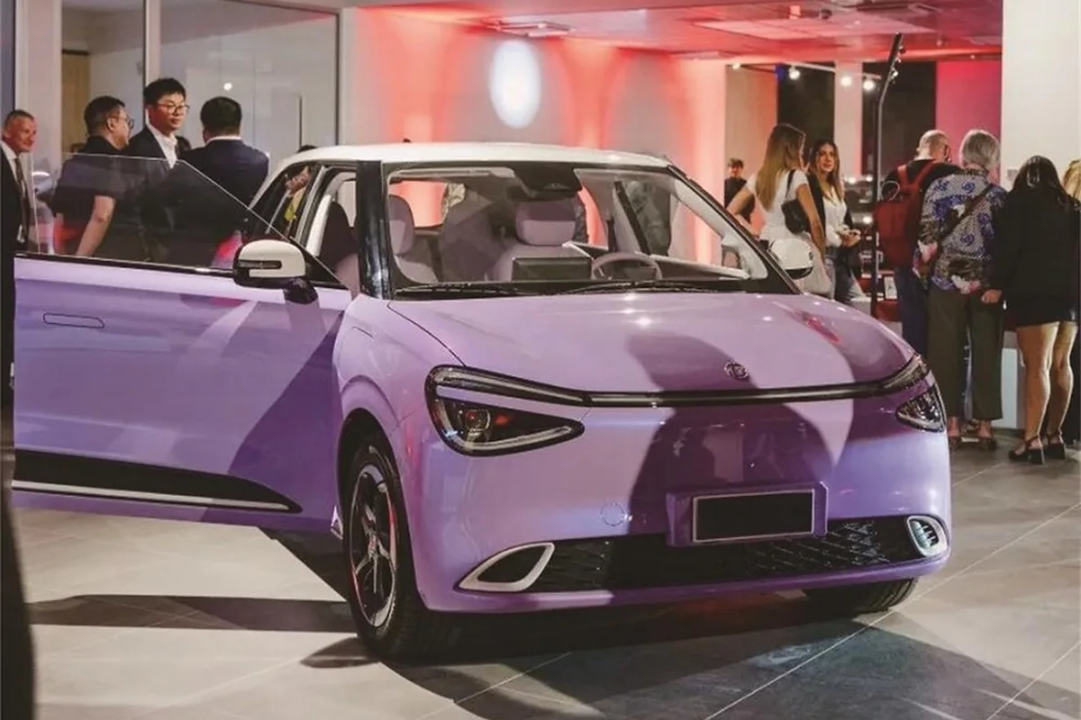 Automóvil compacto Dongfeng de color violeta con la puerta delantera izquierda abierta, expuesto en un salón con varios asistentes.