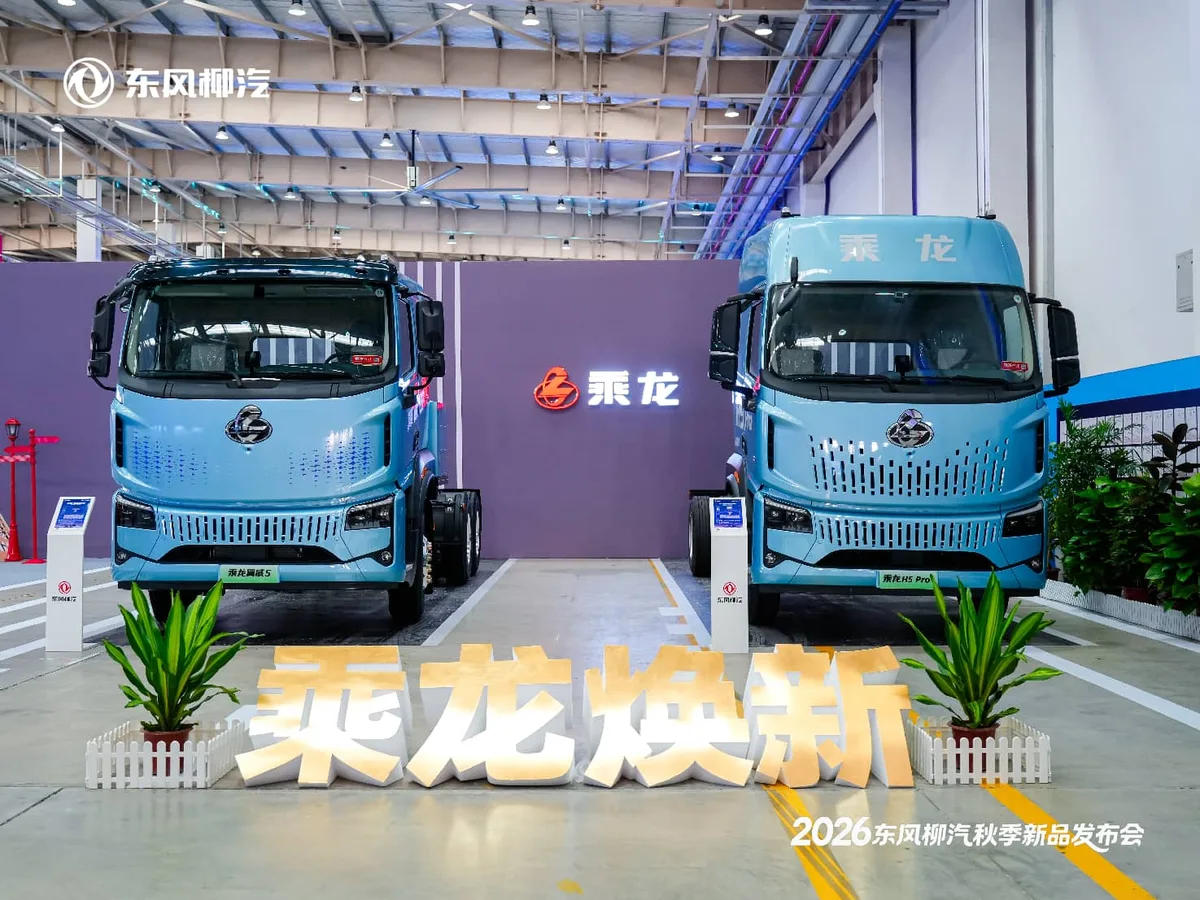 Dos camiones Chenglong de cabina azul claro, exhibidos de frente en una presentación de Dongfeng Liuzhou dentro de una nave industrial.