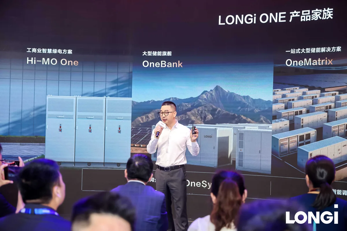 Un ponente presenta la gama LONGi ONE ante una pantalla con los productos Hi-MO One, OneBank y OneMatrix, durante un evento empresarial.