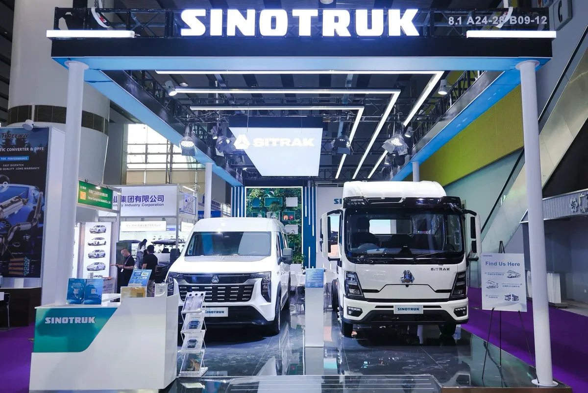 Estand de SINOTRUK en una feria comercial, con una camioneta blanca y un camión SITRAK expuestos
