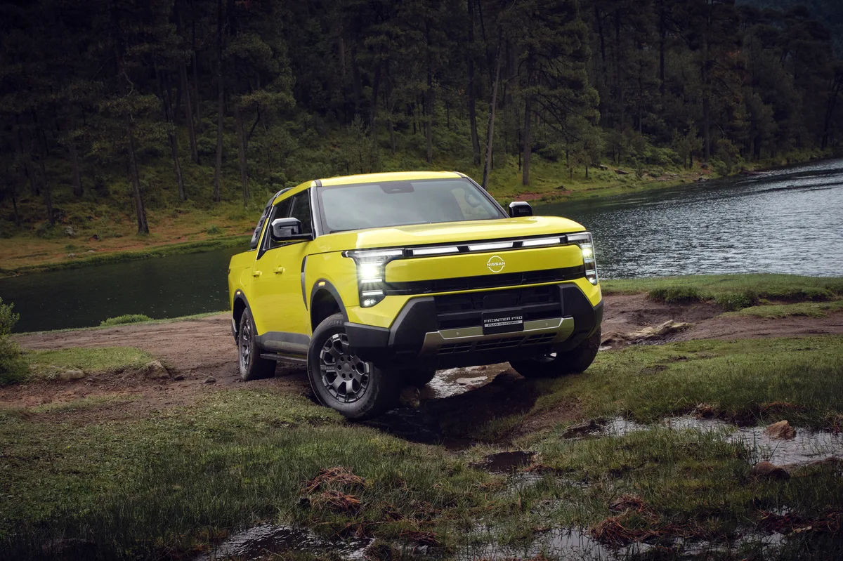 Pickup Nissan Frontier Pro híbrida enchufable amarilla, vista de frente y de lado junto a un lago, con un bosque al fondo.
