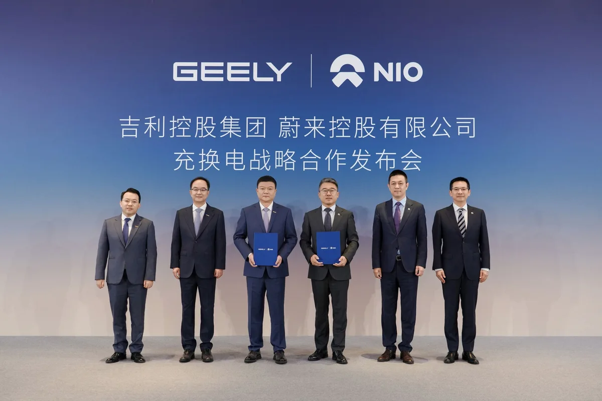 Seis representantes de Geely y NIO posan ante un fondo azul con los logotipos de ambas compañías; dos sostienen carpetas durante la presentación de su alianza.