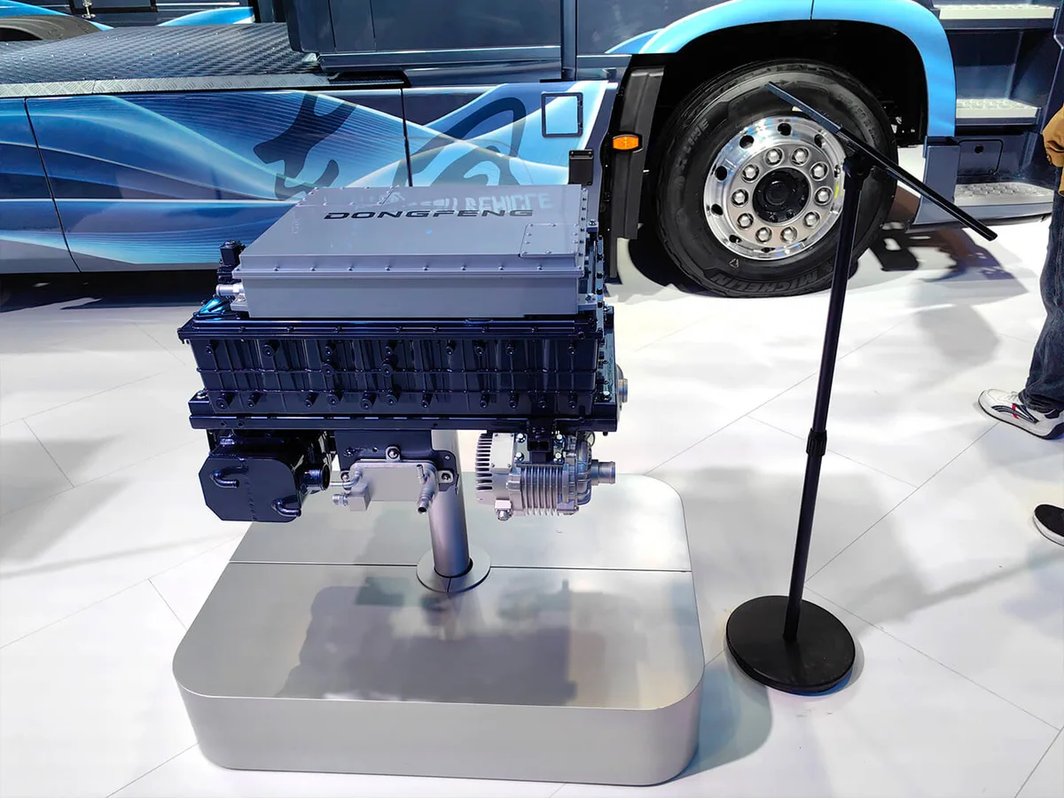 Módulo de pila de combustible Dongfeng exhibido sobre un soporte, delante de un camión azul en una exposición de vehículos comerciales.