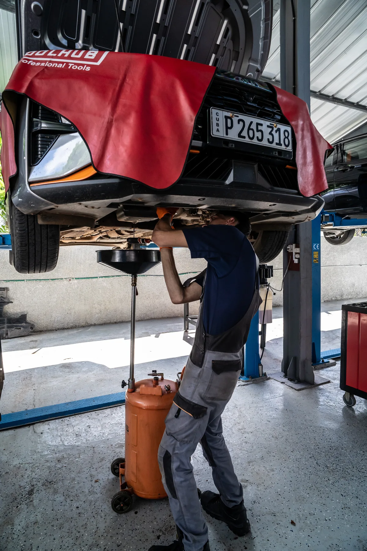 Mecánico retira aceite usado del motor de un automóvil elevado durante una operación de cambio de aceite en un taller.