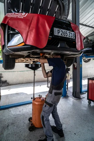 Mecánico retira aceite usado del motor de un automóvil elevado durante una operación de cambio de aceite en un taller.