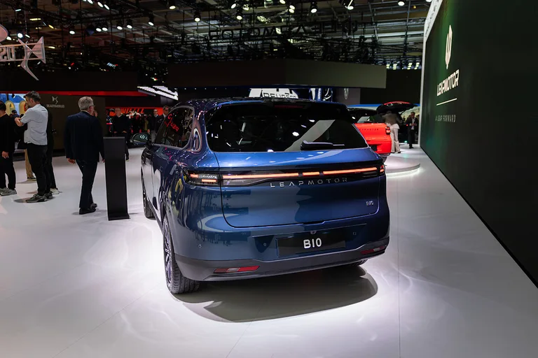 Vista trasera de un Leapmotor B10 azul expuesto en un salón del automóvil, con visitantes y otros vehículos al fondo.