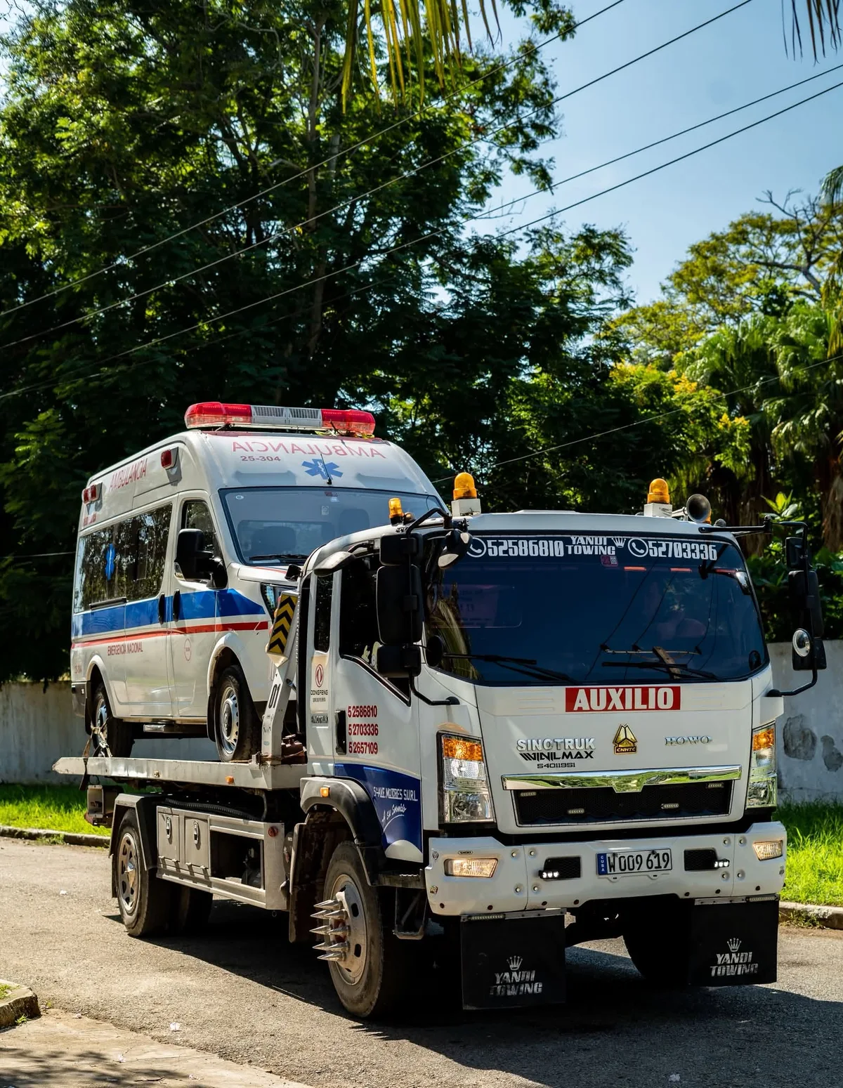 Grúa de plataforma de 5ta Avenida Motores que transporta una ambulancia en una calle de La Habana.