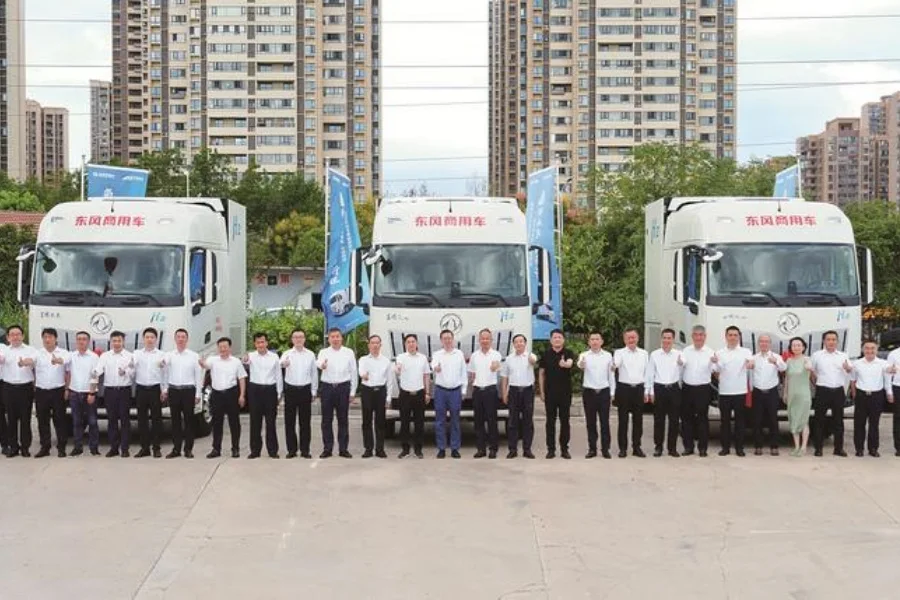 Tres camiones Dongfeng blancos alineados durante un acto de entrega en China, con representantes de las empresas posando delante.