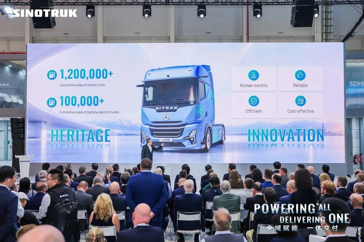 Asistentes a una presentación de Sinotruk frente a una pantalla gigante que muestra un camión eléctrico SITRAK azul.
