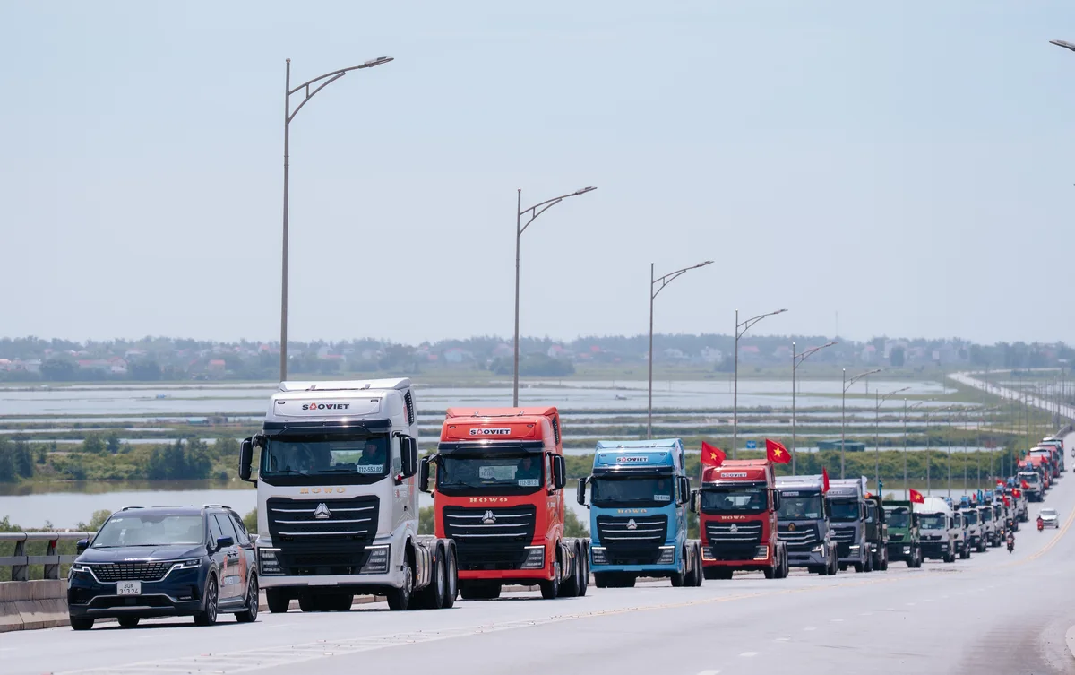 Convoy de camiones HOWO de Sinotruk, blancos, rojos y azules, circulando por una carretera con banderas de Vietnam.