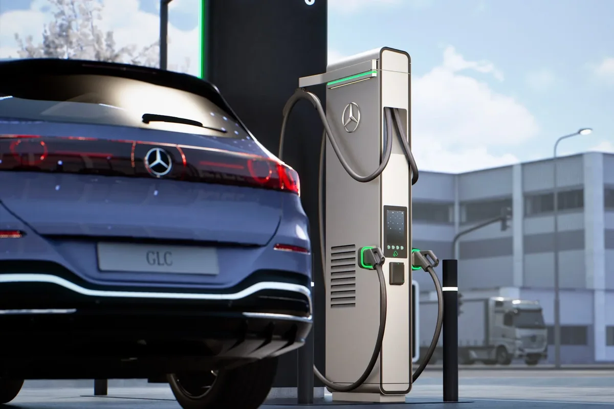 Vista trasera de un Mercedes-Benz GLC eléctrico azul grisáceo junto a una estación de recarga con el emblema de la marca.