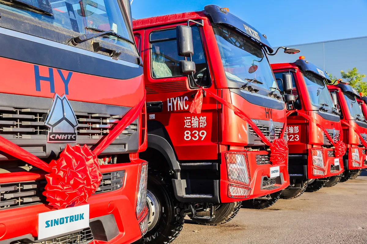 Fila de camiones pesados Sinotruk rojos, vistos de frente y de tres cuartos, con grandes lazos rojos durante una ceremonia de entrega.