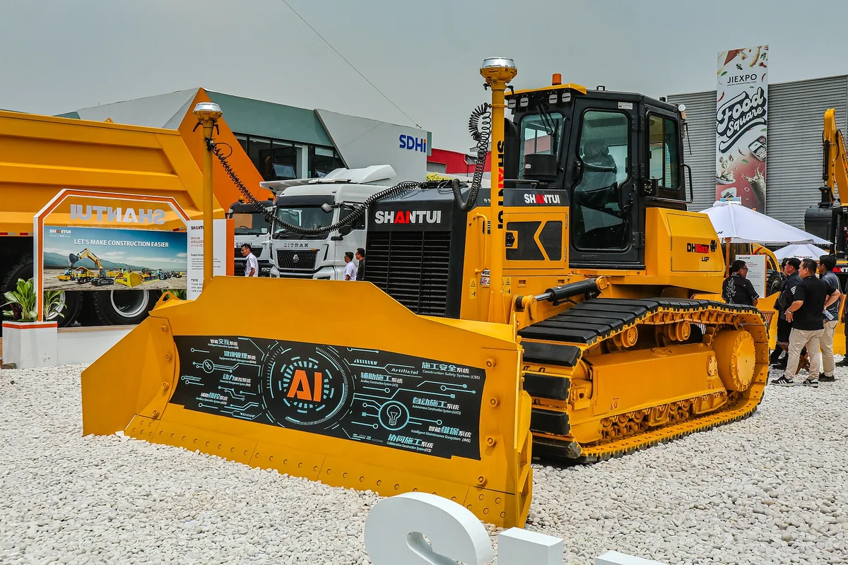 Bulldozer amarillo de orugas Shantui, con un panel alusivo a inteligencia artificial en la hoja frontal, expuesto en una feria de maquinaria en Indonesia.