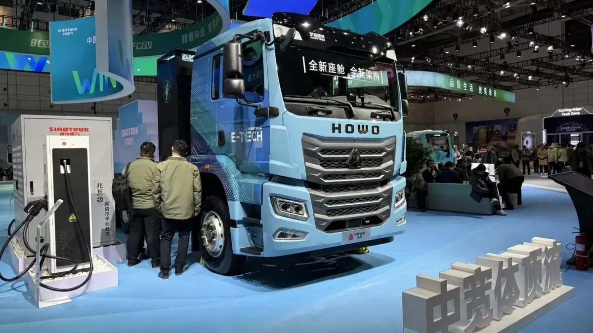 Camión eléctrico Sinotruk HOWO E-TECH azul exhibido en una feria, junto a un cargador y visitantes.