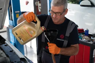 Mecánico con uniforme Dongfeng vierte fluido ATF para transmisión desde un envase a un embudo durante una operación de mantenimiento.