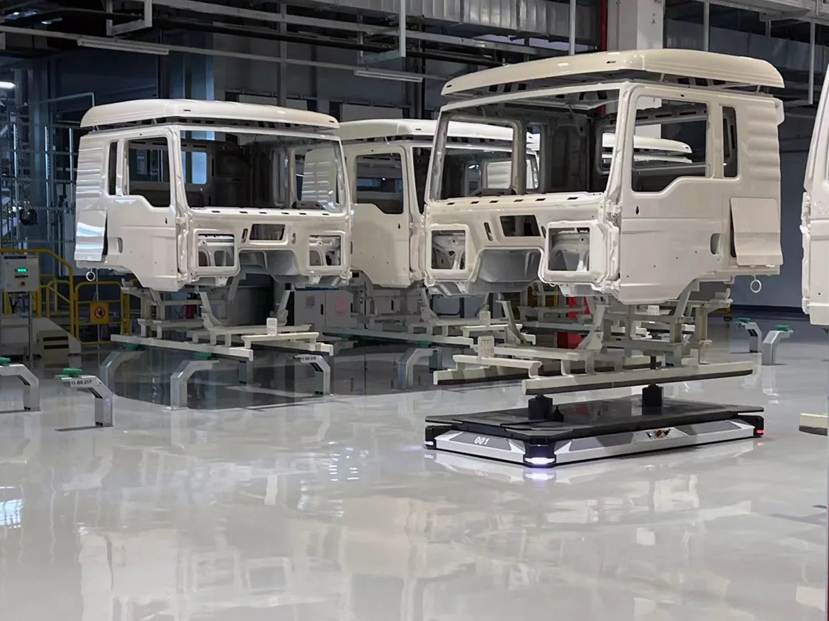 Tres cabinas blancas de camiones Sinotruk en una planta industrial, una de ellas sobre una plataforma móvil autónoma de baja altura.