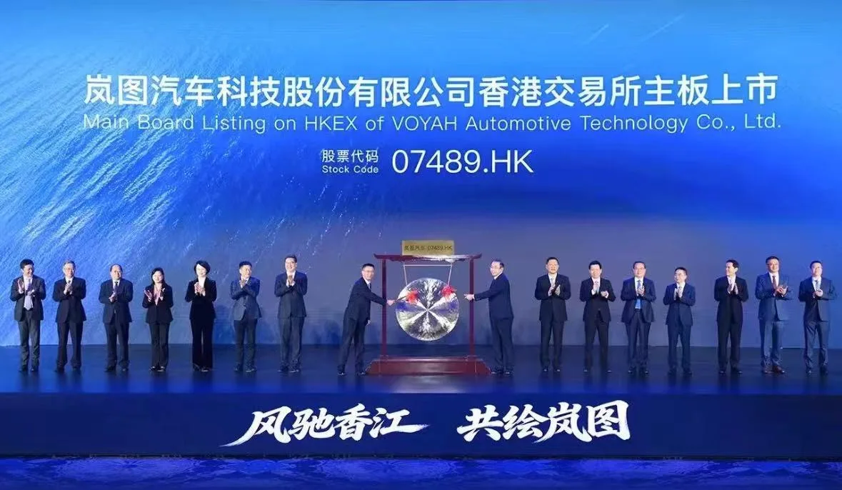 Representantes de VOYAH sobre un escenario azul durante su ceremonia de cotización en Hong Kong, con el código bursátil 07489.HK visible al fondo.